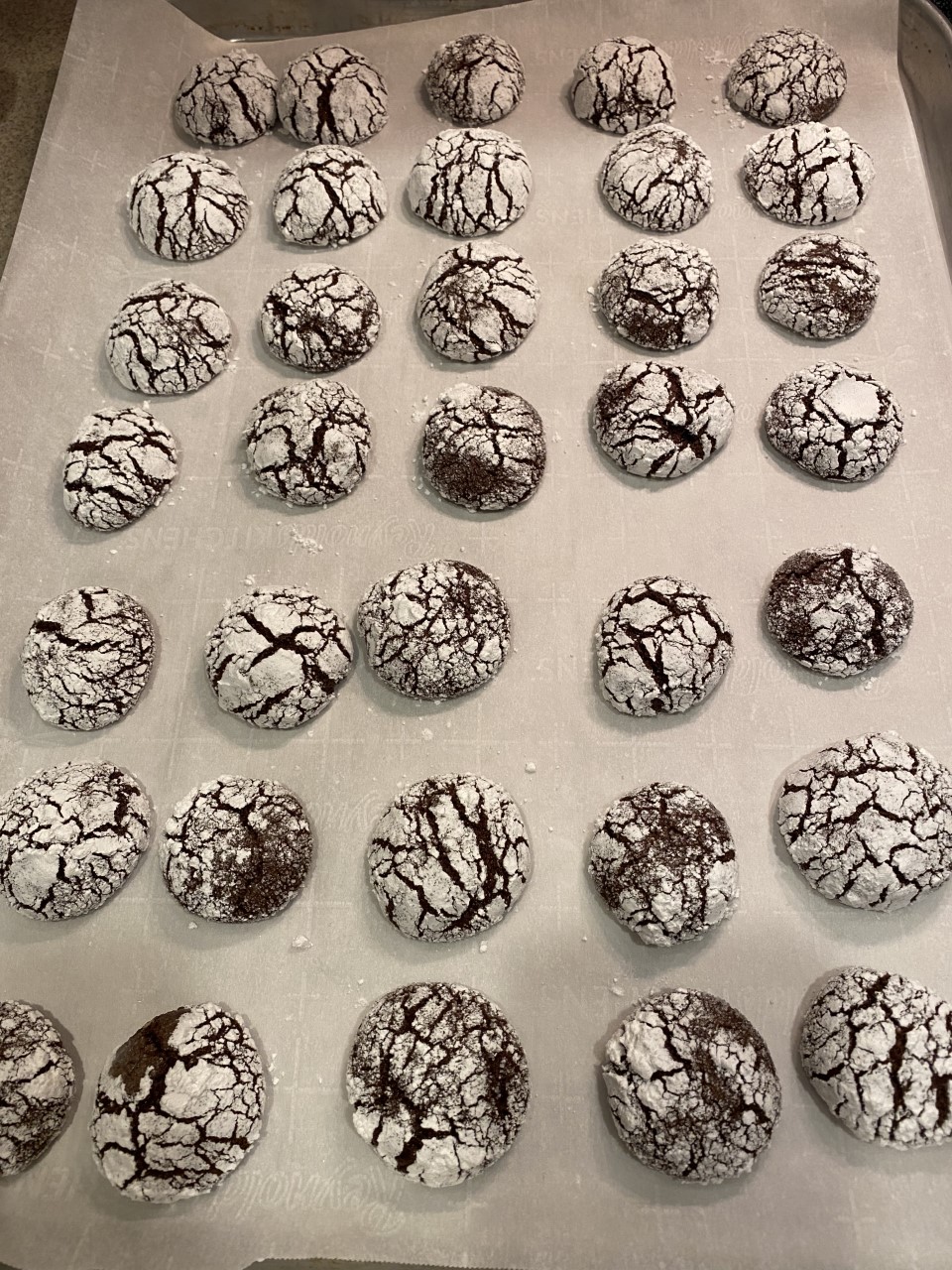 The finished chocolatey, fudgy holiday crinkle cookies on a sheer of parchment, evenly spaced, and looking delicious!