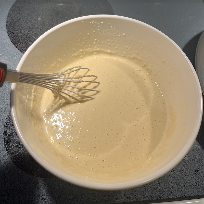 A bowl of smooth batter with a whisk in it