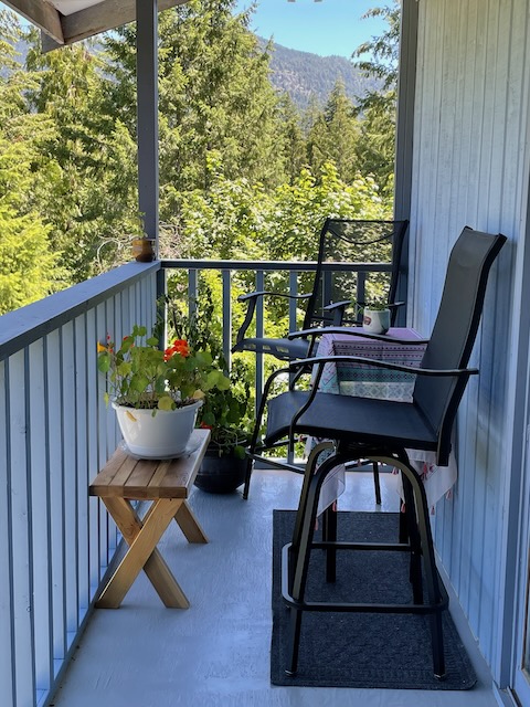 A comfortable balcony featuring a chair, a small bench, a potted plant. In the background are trees.