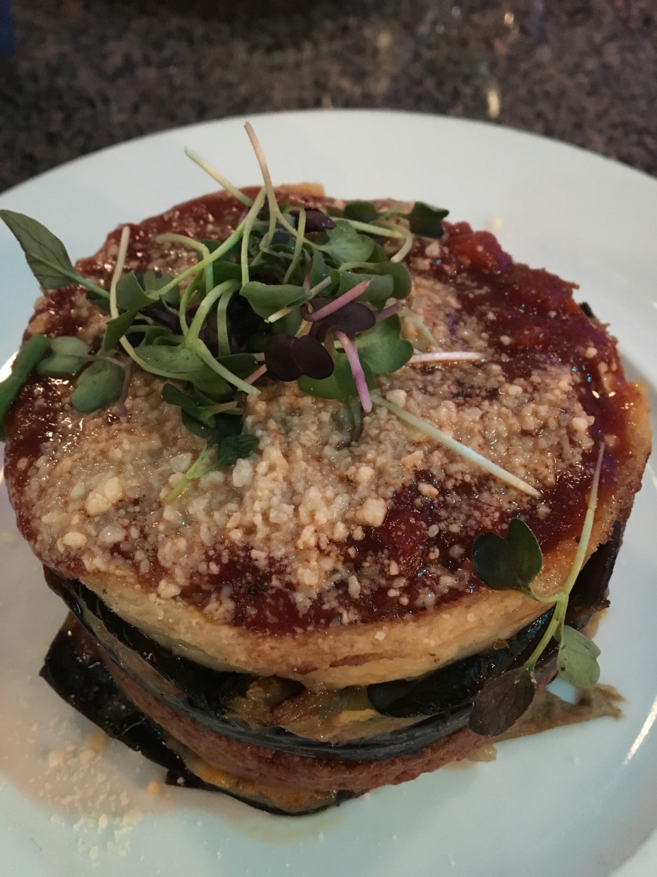 Layers of eggplant, meat sauce, and cheese topped with béchamel and a sprig of greens for garnish