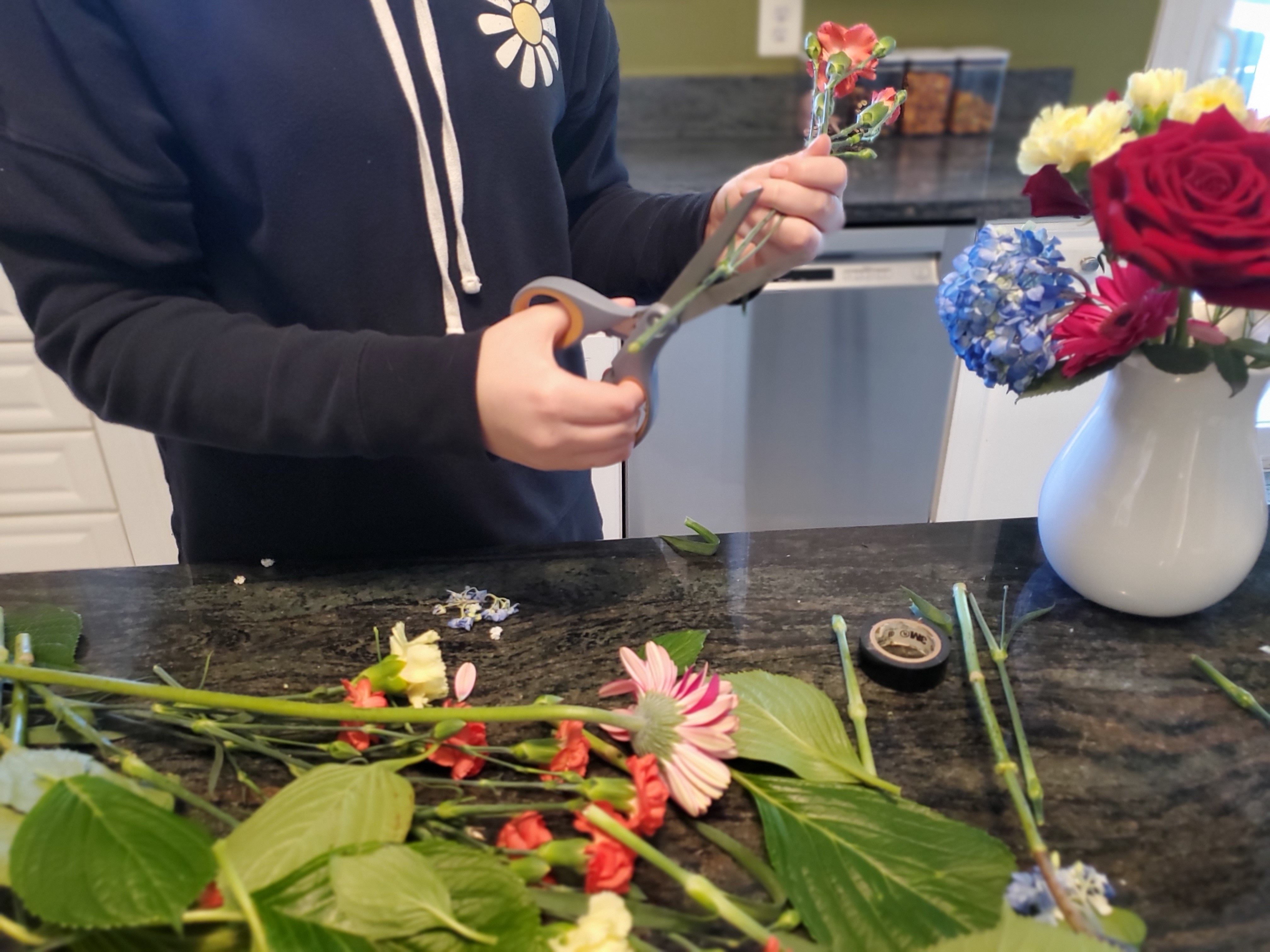 A person in a hoodie cutting the stems of flowers at a 45 degree angle
