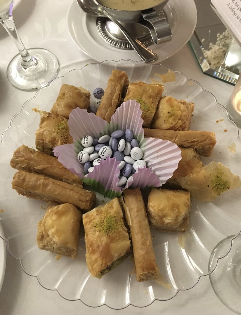 Delicious baklava in various shapes arranged on a clear plate with custom, wedding themed M&Ms in the centre in a paper cupcake liner.