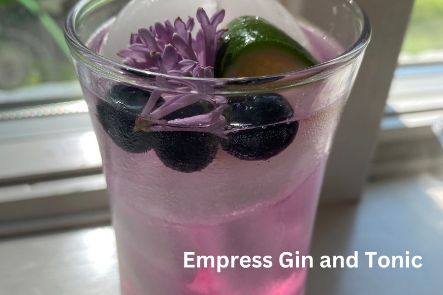 A clear glass with a purple liquid, garnished with ice, berries, and lilac.